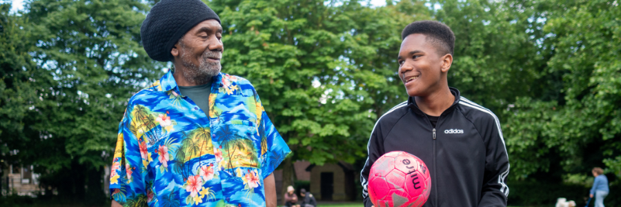 A photo of an older person with a young person with a football in a park