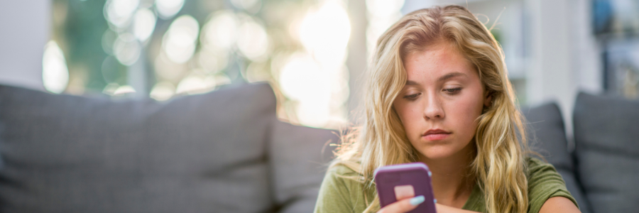 A photo of a young person scrolling on their phone while sitting on the sofa
